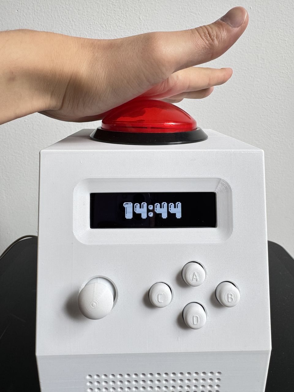 A hand striking the 100 mm illuminated dome button on the top face of the clock