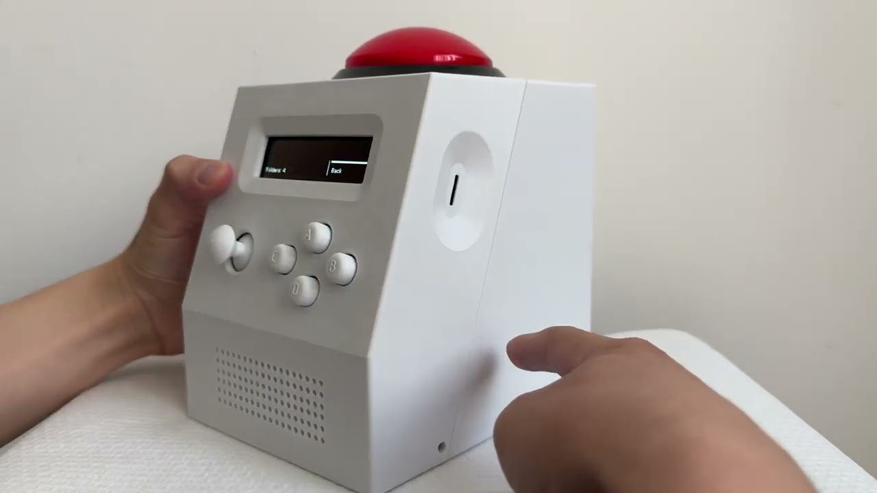 A CinderClock held in both hands on a desk, the display showing a file browser and the red dome button lit above it